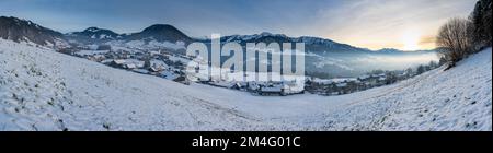 Winterliches Panorama mit verschneiter Landschaft, Blick über Dorf im Winter mit Schnee auf Wiese und Wälder, Berge des Bregenzerwald im Hintergrund, Foto Stock