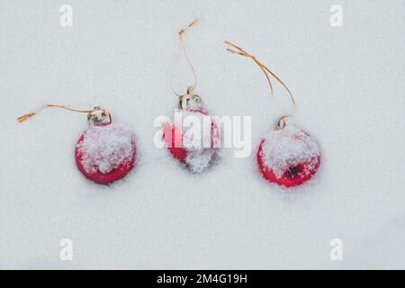 Concetto della cartolina con baubles di Natale coperto di neve, tre baubles rossi Foto Stock