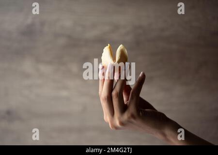 Una mano femminile che tiene un biscotto di fortuna con lo sfondo di legno con lo spazio della copia Foto Stock