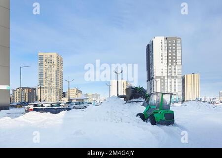 Il trattore per la pulizia dalla neve libera i percorsi. macchina per la rimozione della neve in azione. Il caricatore frontale rimuove tonnellate di neve dai moderni blocchi di strade pianeggiate del distretto. Foto Stock