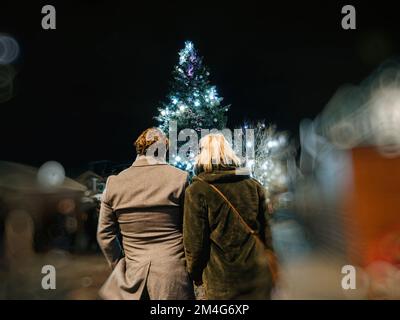 Vista posteriore di coppia reale irriconoscibile ammirando il mercato di natale con alto abete illuminato nella piazza centrale della città di Strasburgo, Alsazia, Francia, Foto Stock