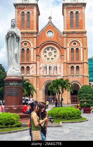 Turisti asiatici con fotocamera che scattano foto di fronte alla Cattedrale di Notre Dame, Saigon, Vietnam Foto Stock