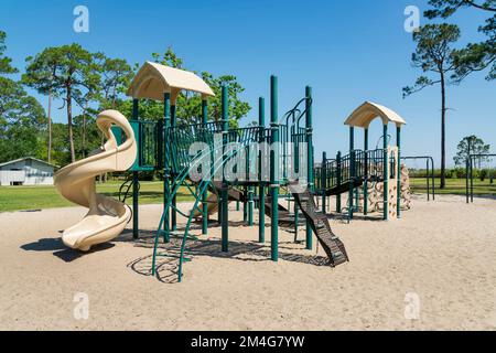 Destin, Florida- Parco giochi con ostacoli e scivoli contro la vista di un campo e alberi. Parco giochi su una sabbia contro il cielo blu chiaro backgroun Foto Stock