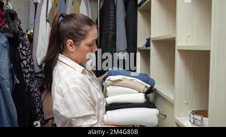 Donna dai capelli castani smista vestiti che mettono su mensole in armadio  di legno. Lady si prende cura degli indumenti e fa lavori domestici nel  proprio armadio a muro Foto stock - Alamy