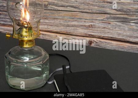 Un primo piano di una vecchia lampada a olio di uragano antico e in fiamme con libro chiuso su un tavolo di legno Foto Stock