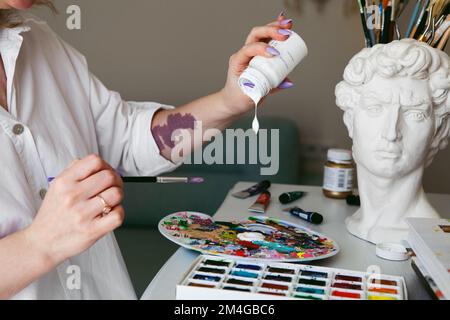 L'artista femminile con il marchio di nascita sulla sua mano mescola vernice acrilica gocciolante sulla tavolozza. La donna si sta preparando a dipingere l'immagine Foto Stock