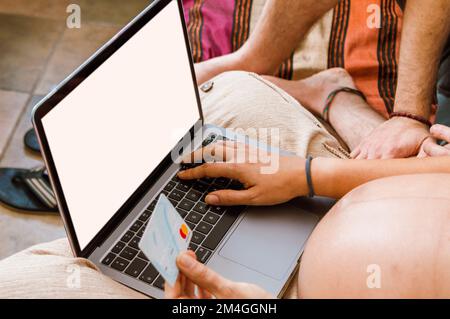 Donna adulta incinta irriconoscibile seduta con il suo laptop e una scheda che acquista prodotti neonatali online, digitando i dettagli della scheda. Foto Stock