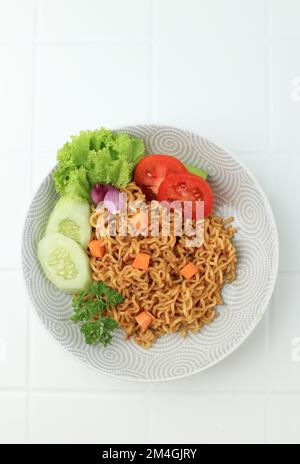 Fried Noodle Indomie Goreng, indonesiano popolare Instant Noodle. Servito con cetriolo e pomodoro. Vista dall'alto Foto Stock