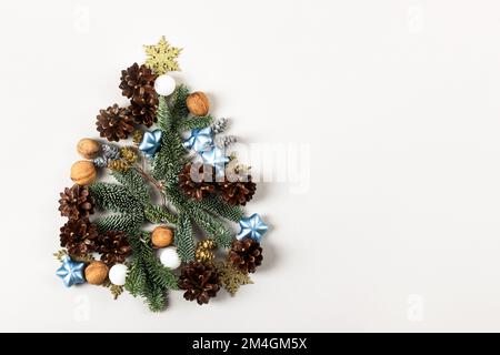 Composizione creativa di Natale a forma di albero di Natale su sfondo grigio, costituita da coni di pino, rami di un albero di Natale, ornamento Foto Stock