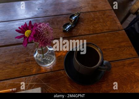 tazza di caffè tavolo di legno in vaso di sfondo con fiori viola nella vegetazione sfondo e luce naturale messico latino-americana Foto Stock