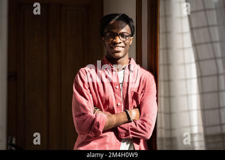 Felice ragazzo nero studente millenario in piedi in soleggiato stanza sorridendo alla macchina fotografica, godendo la vita dormitorio Foto Stock