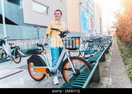 Donna prende una bicicletta a noleggio in un parcheggio per biciclette Foto Stock