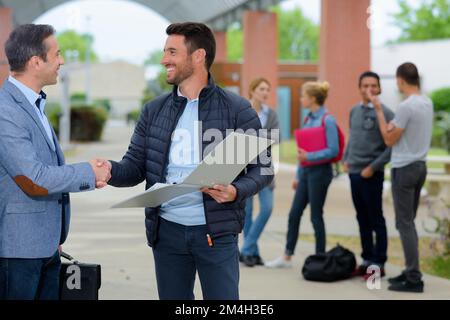 due uomini maturi che scuotono le mani sugli studenti del campus in background Foto Stock