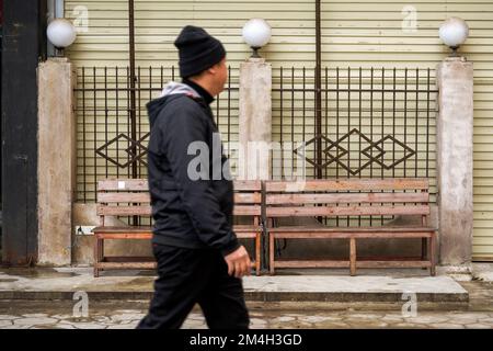 Una persona cammina oltre le panchine di legno fatiscenti nel vecchio quartiere Foto Stock