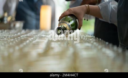 Una mano di donna con una bottiglia di champagne che la versa in bicchieri Foto Stock
