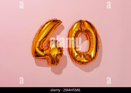 due palloncini dorati a forma di numero che formano il numero 40 su uno sfondo rosa Foto Stock