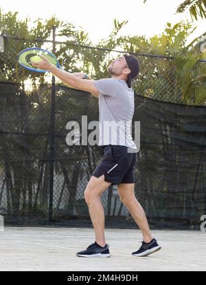 Giovane uomo portatore di berretto gioca a tennis all'aperto. Foto Stock