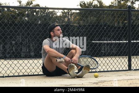 Uomo tennista seduto sul campo da tennis e in attesa del suo turno per giocare a tennis. Foto Stock
