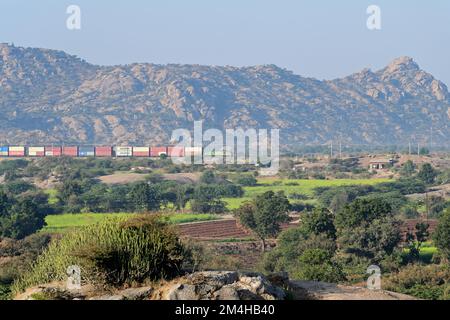 Green Indian Railways locomotiva elettrica che trasporta il treno merci container attraverso l'aspro paesaggio di Jawai Foto Stock