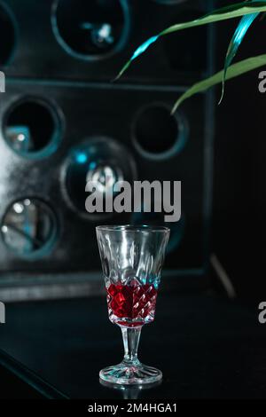 primo piano di un piccolo bicchiere con una bevanda rossa, collocato sul bar, sullo sfondo un banco di esposizione di liquori Foto Stock