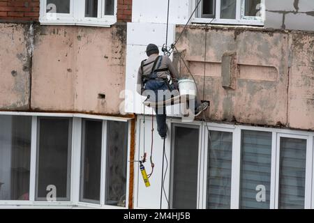 Tiraspol, Moldova - 10 dicembre 2022: Costruttore di alta quota isola la facciata di un edificio di appartamenti con plastica espansa. Casa isolante aerata Foto Stock