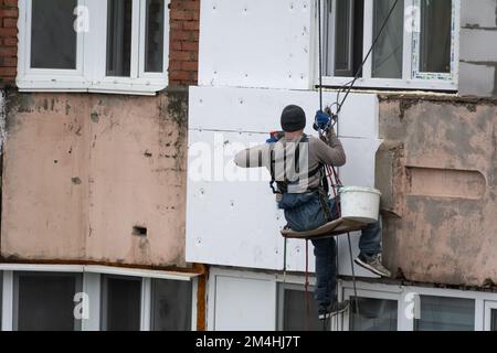 Tiraspol, Moldova - 10 dicembre 2022: Costruttore di alta quota isola la facciata di un edificio di appartamenti con plastica espansa. Casa isolante aerata Foto Stock