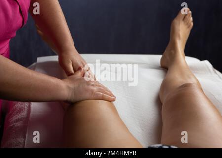 Massaggiatrice femminile che effettua un massaggio rilassante alle gambe ad una ragazza sul divano in una spa Foto Stock