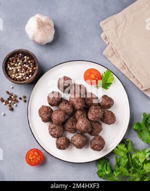 Polpette fritte su un piatto bianco su sfondo blu con erbe fresche, pomodori e spezie. Polpette di carne cotte in forno. Il concetto di sano Foto Stock