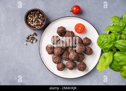Polpette fritte su un piatto bianco su sfondo blu con erbe fresche, pomodori e spezie. Polpette di carne cotte in forno. Il concetto di sano Foto Stock