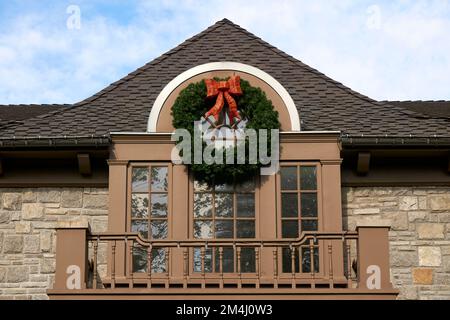Grande corona di Natale verde tradizionale con arco rosso che decorano la parte anteriore di una casa Foto Stock