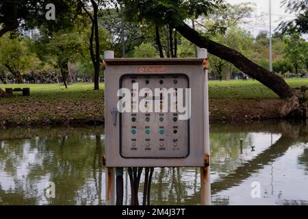 Unità di controllo dell'aeratore di aspirazione accanto a un laghetto nel parco Lumpini, Bangkok, Thailandia. Con cartello rosso non fumatori in lingua tailandese Foto Stock