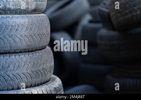 Vecchi pneumatici di gomma usati impilati con pali alti. Rifiuti pericolosi che richiedono il riciclaggio e lo smaltimento. Foto Stock