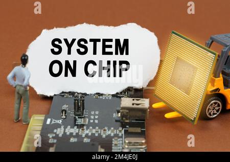 Concetto di computer. Sulla scheda con microcircuiti si trova una lastra di carta con l'iscrizione System on chip. Nelle vicinanze si trova un caricatore di giocattoli con un processore An Foto Stock