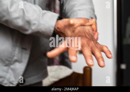 Macro di una mano caucasica anziana con tremori. Effetto sfocato di una doppia esposizione. Concetto di paziente di malattia di Parkinson che cerca di calmare il tremito della mano Foto Stock