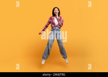 WOW. Full lunghezza del corpo colpo di sorpresa asiatica lady jumping, scioccato da notizie o offerta, sfondo giallo studio Foto Stock