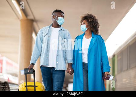 Viaggi pandemici. Coppia afroamericana indossando maschere mediche a piedi alla stazione ferroviaria Foto Stock