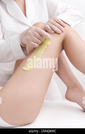 Primo piano del cosmetologist che rimuove i capelli sulle gambe delle donne usando la cera calda. Rapido movimento improvviso di stoffa con cera calda verde professionale salone di bellezza Foto Stock