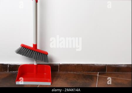 Paletta con scopa su pavimento piastrellato vicino alla parete Foto Stock