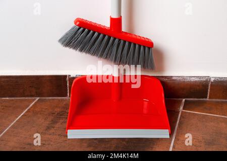 Paletta con scopa su pavimento piastrellato vicino alla parete Foto Stock
