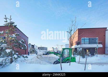 Il trattore per la pulizia dalla neve libera i percorsi. macchina per la rimozione della neve in azione. Il caricatore frontale rimuove tonnellate di neve dai moderni blocchi di strade pianeggiate del distretto. Foto Stock