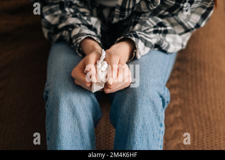 Primo piano vista ad angolo alto di irriconoscibile donna piangente che tiene i tessuti di carta in mano e nervosamente rummaging attraverso di loro a casa. Foto Stock
