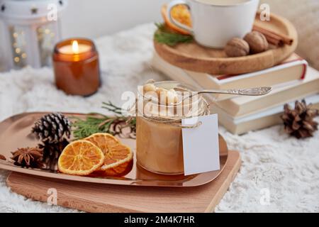 Cibo di Natale. Caramello alla nocciola fatto in casa ed estetico in vasetto di vetro con etichetta mockup e tazza di cacao. Foto Stock