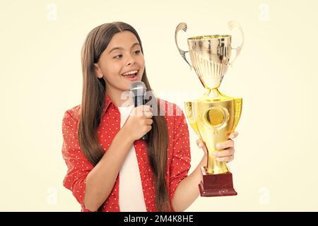 Ragazza adolescente con la tazza di vincita. Teen che tiene un discorso del microfono del trofeo. Bambino vincitore del capretto ha vinto la concorrenza, celebrando il successo e la vittoria. Foto Stock