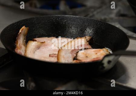 Fettine di pancetta tagliate a fette spesse che friggono in una padella di ghisa Foto Stock