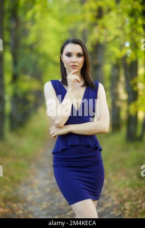 Donna in abito blu che cammina lungo il vicolo autunnale tiglio albero. Percorso sotto gli alberi gialli con foglie autunnali in caduta. Giorno autunnale soleggiato. I raggi del sole Foto Stock