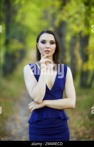 Donna in abito blu che cammina lungo il vicolo autunnale tiglio albero. Percorso sotto gli alberi gialli con foglie autunnali in caduta. Giorno autunnale soleggiato. I raggi del sole Foto Stock