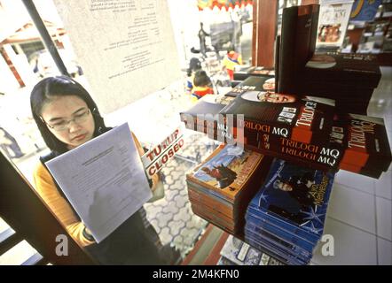 Una donna è fotografata da dietro il vetro di una libreria gestita da Manajemen Qolbu (mq), una filiale di gestione di Daaut Tauhiid, un'istituzione islamica fondata dal famoso predicatore islamico indonesiano, KH Abdullah Gymnastiar, situata a Gegerkalong, Bandung, West Java, Indonesia. Gymnastiar (popolarmente noto come AA Gym), Daarut Tauhiid, e il loro ramo di gestione Manajemen Qolbu (mq), sono riusciti a intensificare il turismo religioso e le attività economiche nella zona di Gegerkalong a Bandung City. Foto Stock