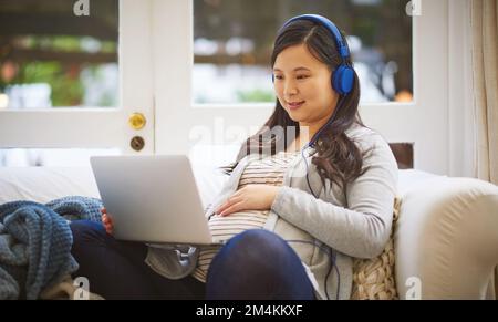 Il mondo online è pieno di tanta conoscenza. donna incinta che indossa le cuffie mentre usa un notebook a casa. Foto Stock