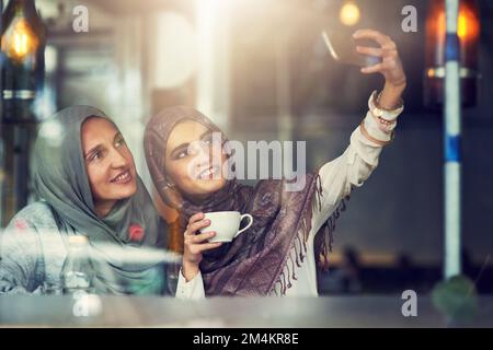 Andiamo insieme come caffè e panna. due donne che scattano selfie con un telefono cellulare in un bar. Foto Stock