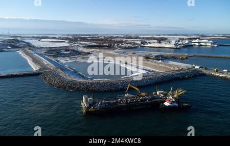 Fehmarn, Germania. 16th Dec, 2022. La fossa di scavo per il portale del tunnel al tunnel di Fehmarnbelt è visibile accanto al porto di lavoro e al porto dei traghetti di Puttgarden (fotografia aerea scattata con un drone). Il tunnel ferroviario e stradale di 18 km collegherà l'isola di Fehmarn e l'isola danese di Lolland dal 2029. Secondo Femern A/S, il costo è di 7,1 miliardi di euro. Credit: Christian Charisius/dpa/Alamy Live News Foto Stock